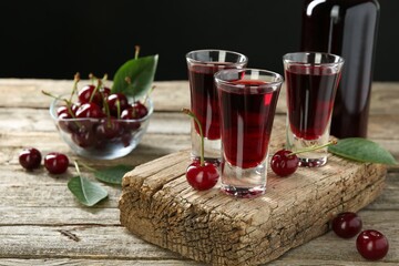 Bottle and shot glasses of delicious cherry liqueur with juicy berries on wooden table
