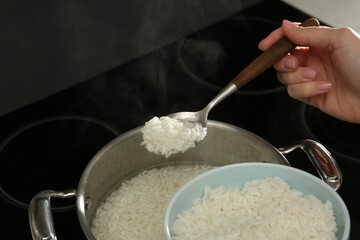 Woman taking boiled rice from pot into bowl, closeup