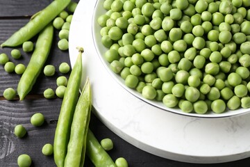 Fresh green peas in bowl and pods on black wooden table, closeup