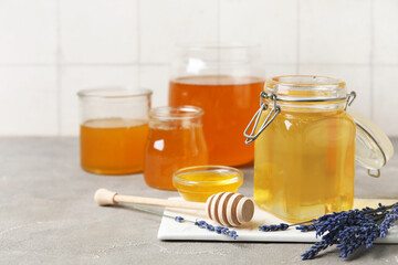Jars, glass and bowl of sweet honey with dipper on grey grunge table