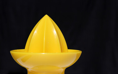 Yellow citrus juicer against a black background