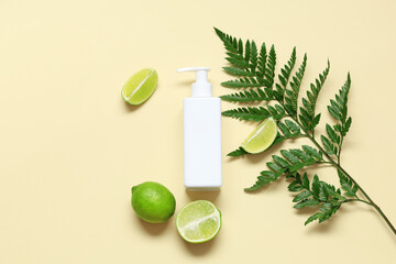 Composition with lime, fern twig and bottle of cosmetic product on yellow background