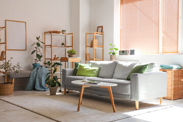 Interior of stylish living room with grey sofa, houseplants, coffee table and shelving unit