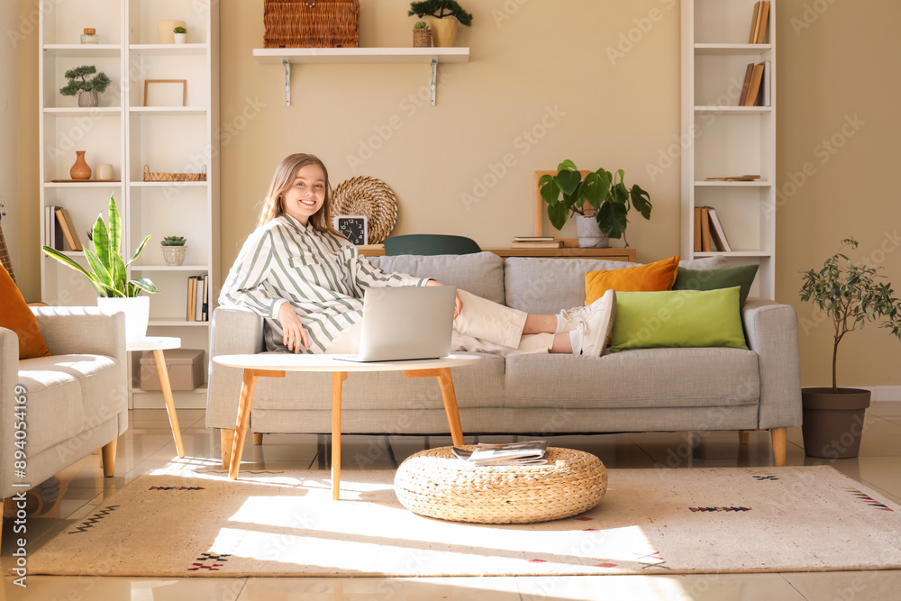 Wall mural Young woman sitting on sofa and working with laptop in living room