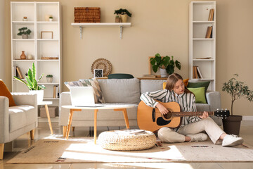 Young woman playing guitar on floor near sofa in living room