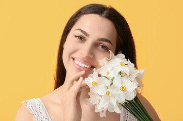 Happy young woman with bouquet of white daffodil flowers on yellow background