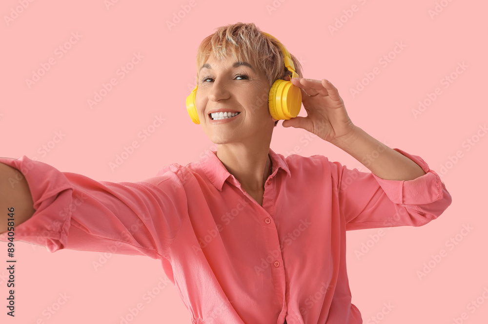 Canvas Prints Mature woman in headphones listening to music on pink background, closeup