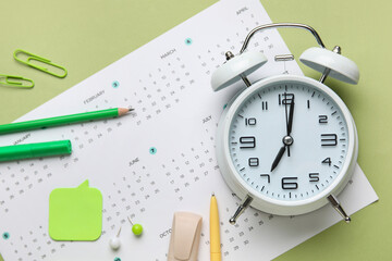 Calendar with alarm clock and office stationery on green background