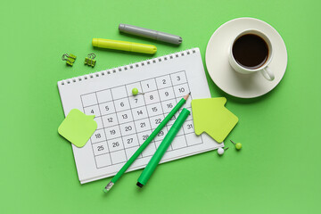 Calendar with cup of coffee and office stationery on green background