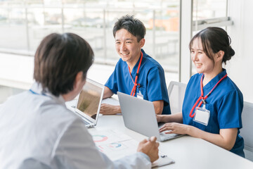 Obraz premium 医局でカンファレンス・打ち合わせ・ミーティングする男女の看護師・技師・作業療法士・理学療法士・医師 
