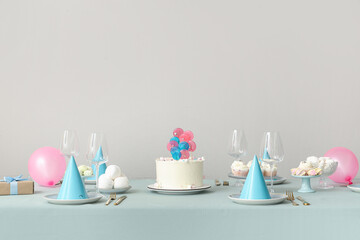 Cake with sweets and dishes for birthday party on table against white wall