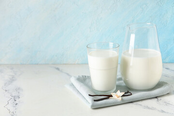 Glass and jug of fresh vanilla milk with sticks and flower on white table