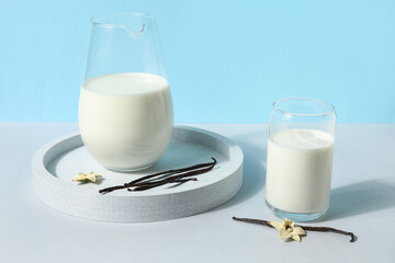 Glass and jug of fresh vanilla milk with sticks and flowers on colorful background