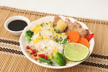 Bowl of tasty rice with vegetables, chicken and soy sauce on bamboo mat
