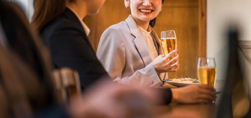 居酒屋・飲み屋のカウンターで部下と楽しくお酒を飲むビジネスウーマン
