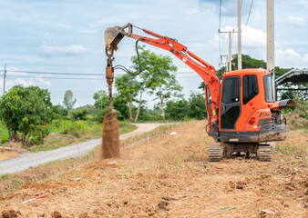 Mini excavator makes holes with auger drill for install pole fence.