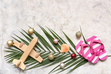 Wooden airplane, kid's flip-flops and palm branch with Christmas balls on white grunge background. Top view