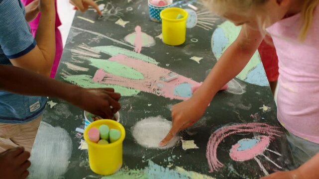 Kids playing, learning and having fun with art, developing their imagination and sketching with chalk. Colorful and creative finger painting of space drawn by children on a chalkboard at school.