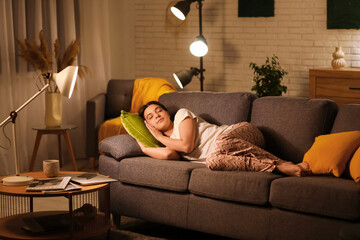 Obraz premium Young woman in pajamas sleeping on cozy sofa in living room at night