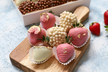 Wooden board with chocolate covered strawberries on light blue background