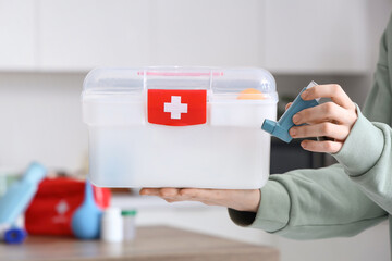Woman with home first aid kit and inhaler in kitchen, closeup
