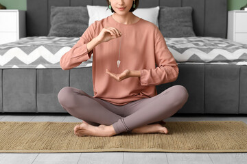 Young woman with pendulum in bedroom