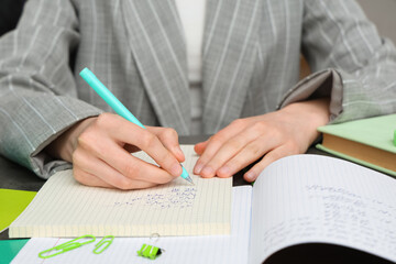 Woman writing math formulas in notebook at table, closeup