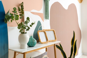 Surfboard, photo frames and vase of eucalyptus branches on bench in room, closeup