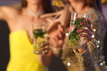 Beautiful young women with glasses of mojito in bar, closeup