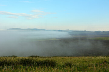 View from the top of the hill to the summer valley, which is covered by dense fog.