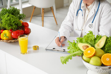 Mature female nutritionist writing on clipboard at table in office, closeup