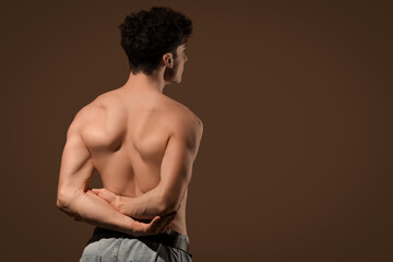 Muscular young man on dark brown background, back view