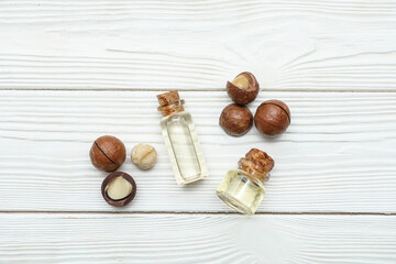 Composition with bottles of macadamia oil and nuts on light wooden background