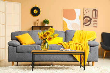 Comfortable sofa and coffee table with sunflowers in interior of living room