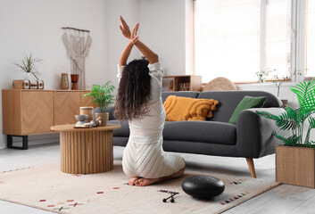 Young woman with Palo Santo on table meditating at home, back view