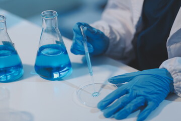 Group of dedicated scientist conduct chemical experiment in medical laboratory, carefully drop precise amount of liquid from pipette into test tube for vaccine drug or antibiotic development. Neoteric