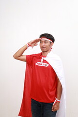 Fototapeta premium Asian young boy with red white ribbon for celebrating Indonesia independence day standing with salute hand gesture while looking side above
