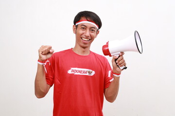 Asian man celebrating Indonesia Independence day, holding megaphone while clenching hand. Isolated on white