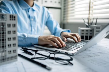 A women architect use laptop and drawing draft on blueprints in the office, working with modern house blueprint floorplans, architectural and construction project concept.