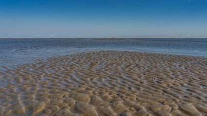 The low tide in the ocean. On the exposed bottom there is a pattern of sandy curved ridges and puddles of water. Tiny silhouettes of people on the horizon. Clear blue sky. Copy space. Madagascar. 