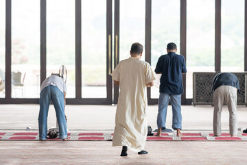 Fifty-something Muslim Malay person in religious attire, wearing a white outfit and a black hat, praying devoutly on a majestic carpet inside a very large mosque in Putrajaya, Malaysia.