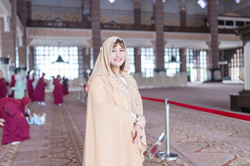 30-something Chinese woman in cream-colored religious attire smiling alone inside very large mosque in Putrajaya, Malaysia.