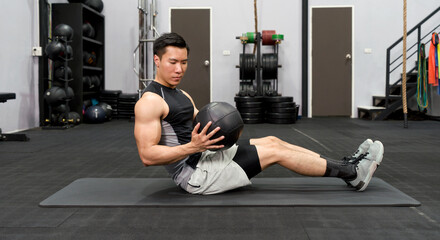 A man exercises with a medicine ball in a gym, focusing on core strength and muscle building.