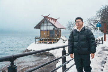 man tourist sightseeing Kansa Shrine and Lake Tazawa in winter. Traveler travel in Semboku city, Akita Prefecture, Japan. Landmark for tourist attraction in Tohoku region. Japan travel and vacation
