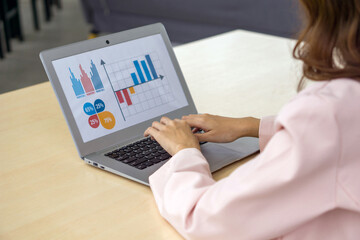 Back view of businesswoman in suit sit at desk in office typing on laptop computer keyboard, making presentation with graph and multicolored chart.