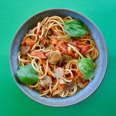 Spaghetti Primavera in a bowl garnished with baby spinach leaves. 