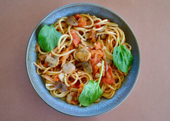 Spaghetti Primavera in a bowl garnished with baby spinach leaves. 