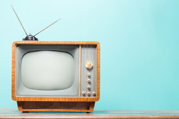 Old television with wooden body, vintage antenna on table front gradient mint blue background. Retro style filtered photo