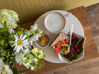 Delicious breakfast served on a wooden bench in the living room - cappuccino, salmon toast, boiled egg, raspberry spinach salad