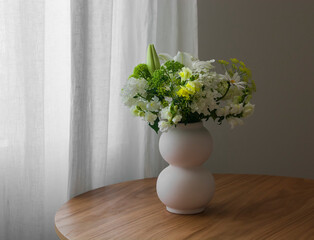 A bouquet of summer flowers in a ceramic vase on a round wooden table in the living room
